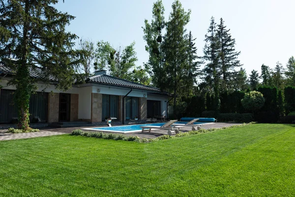 Vue extérieure de la maison moderne, pelouse verte et côté piscine avec chaises longues — Photo de stock