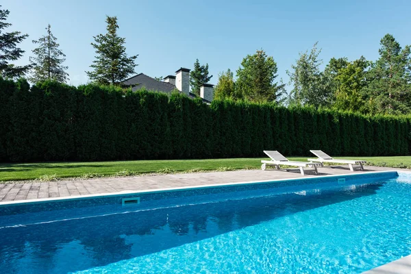 Вид на бассейн с шезлонгами и зеленым забором — стоковое фото