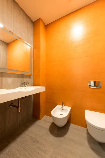 Interior of modern bathroom in orange and white colors with toilet and bidet — Stock Photo