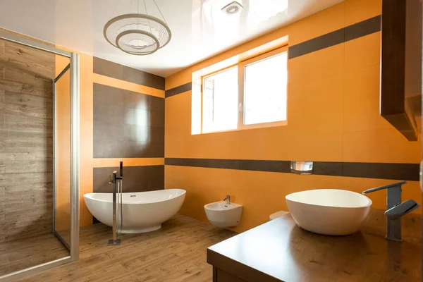 Interior do banheiro em cores laranja e branco com banheira, pia e bidé — Fotografia de Stock