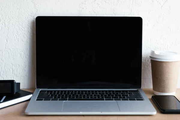 Close-up view of laptop with blank screen, notebook, smartwatch, smartphone and coffee to go  on table — Stock Photo