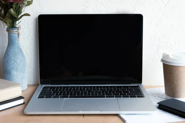 Laptop mit leerem Bildschirm, Zeitung, Smartphone, Coffee to go und Büchern auf dem Tisch — Stockfoto