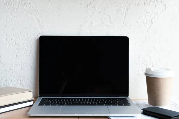 Laptop mit leerem Bildschirm, Bücher, Zeitung, Smartphone und Kaffee zum Mitnehmen — Stockfoto