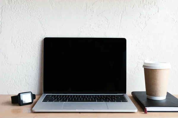 Laptop com tela em branco, smartwatch, notebook e café para ir na mesa — Fotografia de Stock