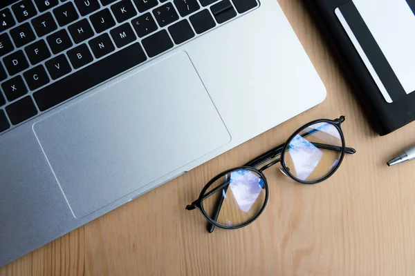 Top view of laptop, eyeglasses, notebook, pen and credit card on wooden table — Stock Photo