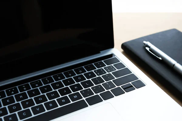 Vista de cerca de la computadora portátil con pantalla en blanco, cuaderno y pluma en la mesa - foto de stock