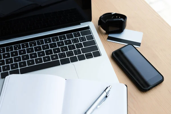 Vista de alto ângulo de laptop, smartwatch, smartphone, cartão de crédito e notebook em branco com caneta na mesa — Fotografia de Stock