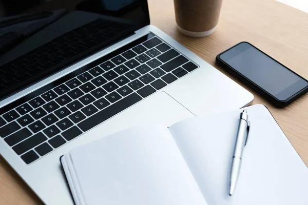 Laptop, smartphone e notebook em branco com caneta na mesa de madeira — Fotografia de Stock