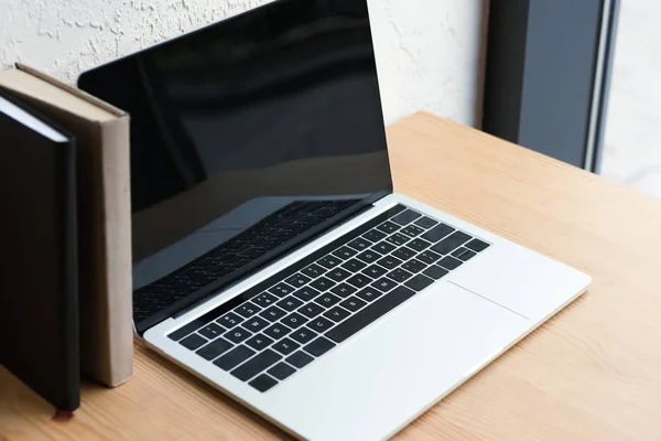 Vista ravvicinata del computer portatile con schermo bianco e libri su tavolo di legno — Foto stock