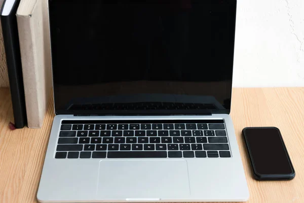 Laptop con pantalla en blanco, libros y smartphone sobre mesa de madera - foto de stock