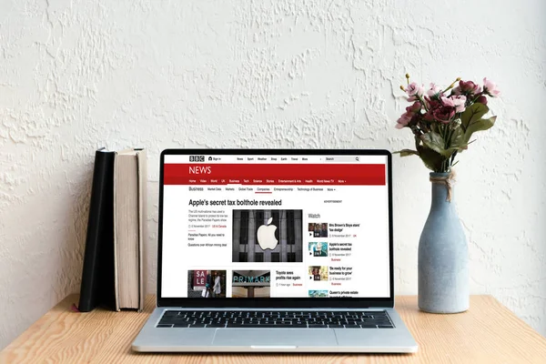 Ordinateur portable avec site de nouvelles bbc à l'écran, livres et fleurs dans un vase sur une table en bois — Photo de stock