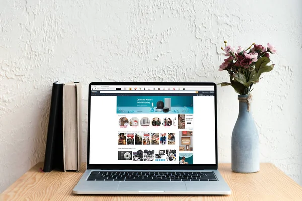 Laptop with amazon website on screen, books and flowers in vase on wooden table — Stock Photo