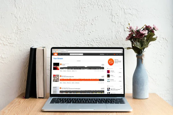 Computer portatile con sito web soundcloud sullo schermo, libri e fiori in vaso su tavolo di legno — Foto stock