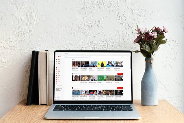 Computer portatile con sito web youtube sullo schermo, libri e fiori in vaso su tavolo di legno — Foto stock