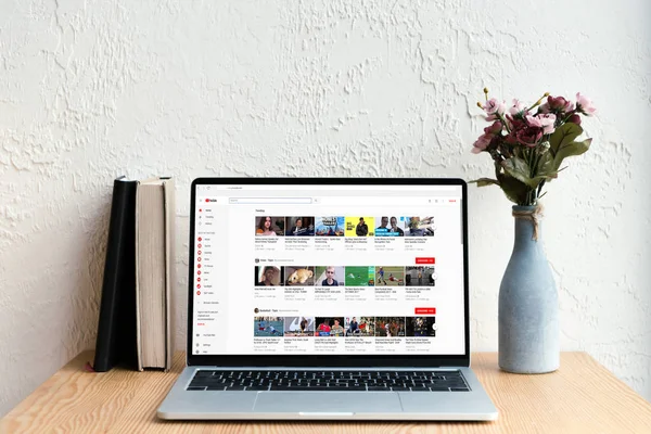 Portátil con youtube sitio web en pantalla, libros y flores en jarrón en mesa de madera - foto de stock