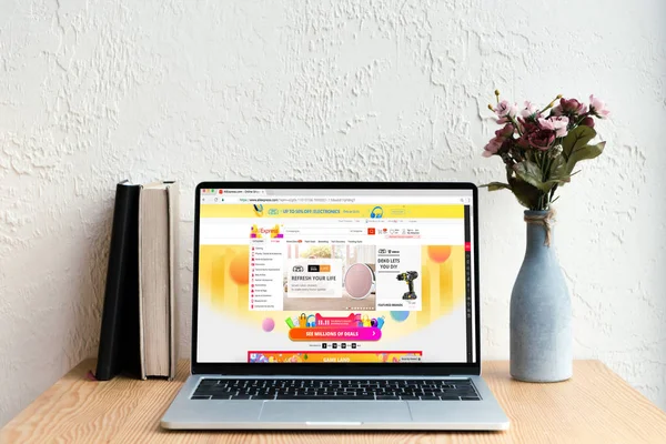 Computer portatile con sito web aliexpress sullo schermo, libri e fiori in vaso su tavolo di legno — Foto stock
