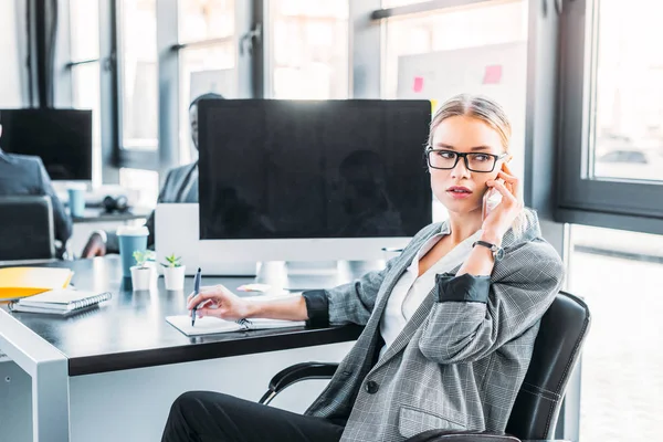 Schöne Geschäftsfrau, die im Büro per Smartphone spricht — Stockfoto