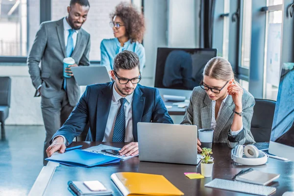 Multicultural businesspeople looking at laptops in office — Stock Photo