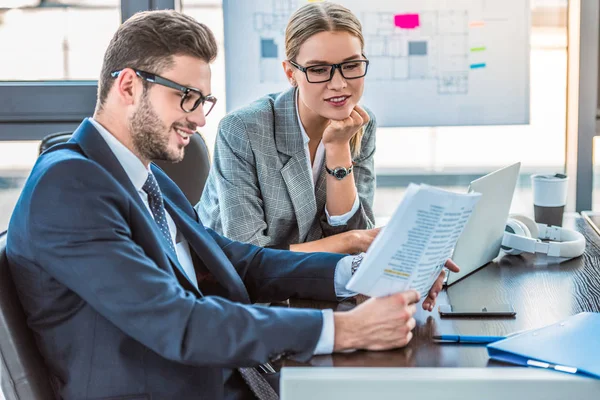 Homme d'affaires souriant et femme d'affaires à la recherche de documents dans le bureau — Photo de stock