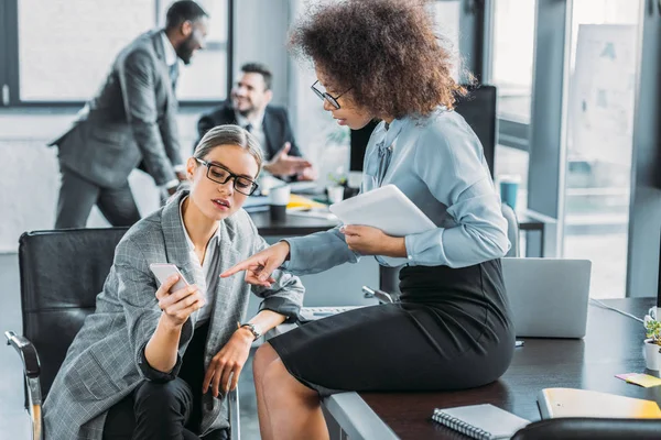 Multicultural businesswomen looking at smartphone in office — Stock Photo