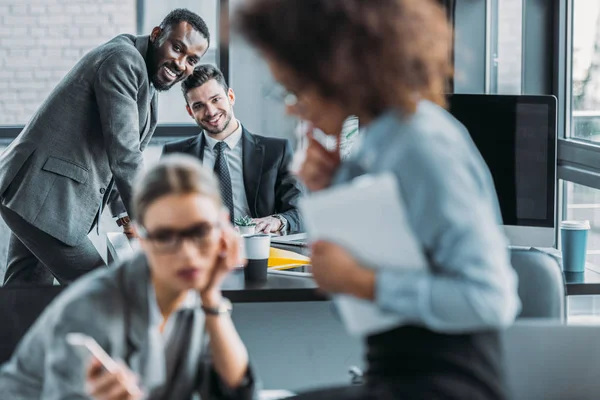 Lächelnde multiethnische Geschäftsleute mit Blick auf Geschäftsfrauen im Amt — Stockfoto