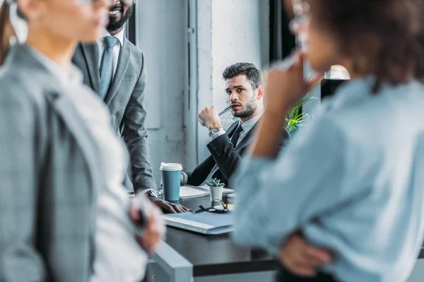 Businessman looking at multicultural colleagues talking in office — Stock Photo