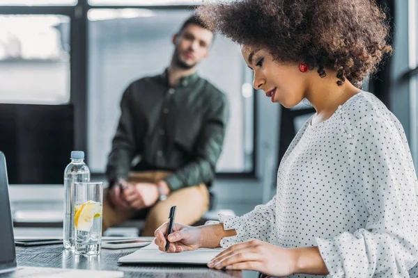 Seitenansicht einer afrikanisch-amerikanischen Geschäftsfrau, die im Büro etwas schreibt — Stockfoto