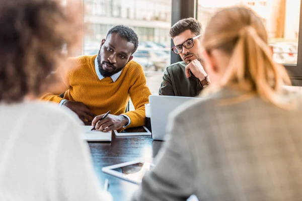 Empresarios multiculturales sentados a la mesa en el cargo - foto de stock