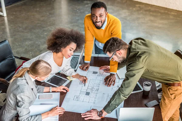 High angle view of multicultural businesspeople looking at blueprint in workspace — Stock Photo
