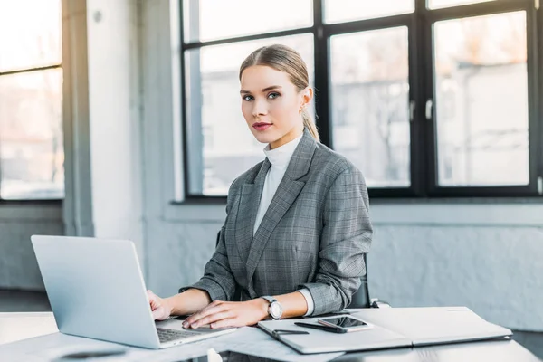 Beautiful businesswoman using laptop in office and looking at camera — Stock Photo