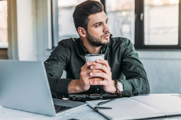 Бизнесмен сидит за столом в офисе и держит чашку кофе — стоковое фото