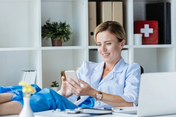 Doctora adulta con piernas en la mesa usando smartphone en la oficina - foto de stock