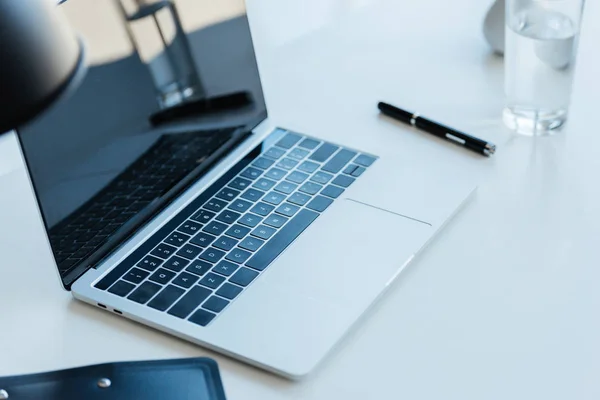 Enfoque selectivo de la computadora portátil con pantalla en blanco en la mesa en la oficina moderna - foto de stock