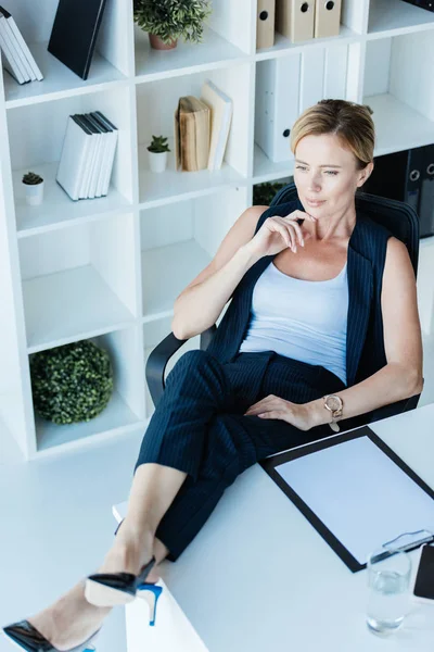 Високий кут зору стомлюючої дорослої бізнес-леді, що сидить з ногами на столі в офісі — стокове фото