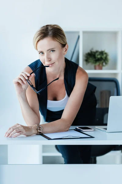 Adult businesswoman holding eyeglasses and looking at camera in office — Stock Photo