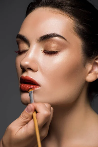 Esthéticienne appliquant du rouge à lèvres sur les lèvres des filles avec pinceau cosmétique, isolé sur gris — Photo de stock
