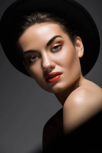 Привлекательная чувственная женщина с макияжем, позирующая в черной войлочной шляпе, изолированная на сером — стоковое фото
