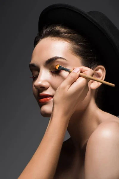 Esteticista aplicando sombras de ojos en la cara de las niñas con cepillo cosmético, aislado en gris - foto de stock