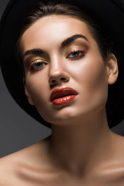 Sensuale giovane donna con trucco posa in feltro nero cappello, isolato su grigio — Foto stock