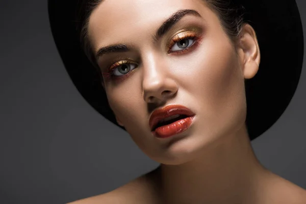 Schönes Mädchen mit Make-up posiert in schwarzem Filzhut für das Mode-Shooting, isoliert auf grau — Stockfoto
