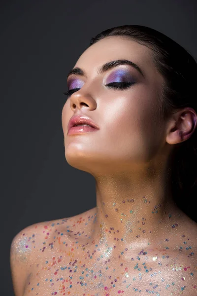 Tender woman with closed eyes posing with makeup and glitter on body, isolated on grey — Stock Photo