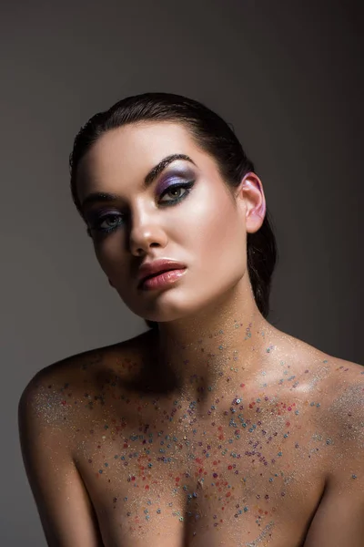 Glamorous young woman posing with glitter on body, isolated on grey — Stock Photo