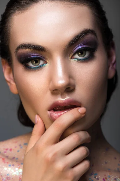 Niña reflexiva posando con glamour maquillaje y brillo en el cuerpo, aislado en gris - foto de stock