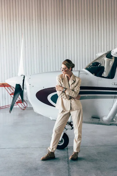 Fashionable woman in sunglasses and jacket posing near aircraft in hangar — Stock Photo