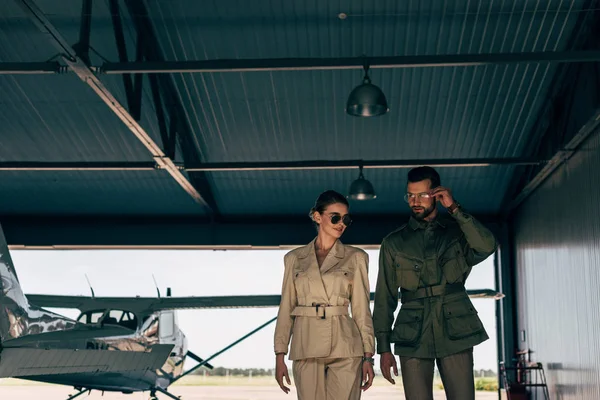Couple in stylish jackets walking near airplane in hangar — Stock Photo