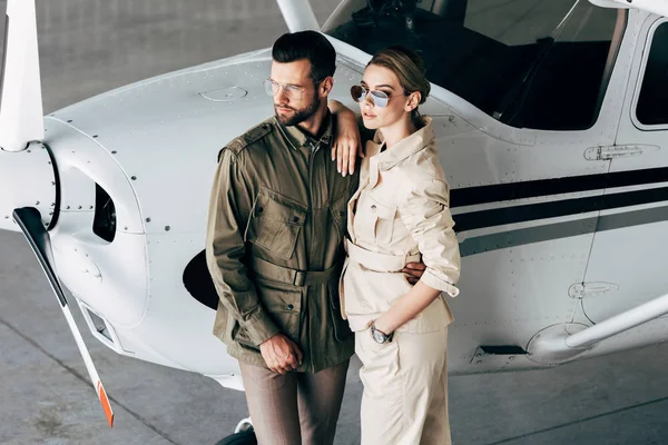 Високий кут зору модна молода пара в стильних куртках, що стоять біля літака — стокове фото