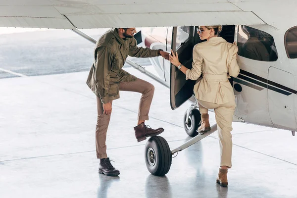 Smiling young man opening door for girlfriend while she boarding in airplane — Stock Photo