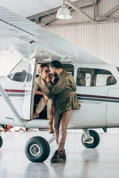 Jeune couple à la mode en vestes se regardant près de l'avion — Photo de stock