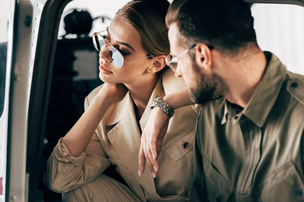 Selektiver Fokus der attraktiven Frau mit Sonnenbrille, die im Flugzeug sitzt, während ihr Freund in der Nähe des Flugzeugs steht — Stockfoto