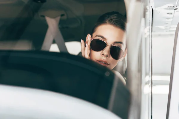 Retrato de hermosa joven en gafas de sol sentado en el avión - foto de stock